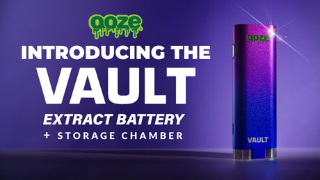 The four Ooze Vault batteries are laying flat on a white wooden table. The green one is out of the package with a cartridge attached and silver atomizer displayed next to the storage compartment. The silver, black and rainbow batteries are in boxes.