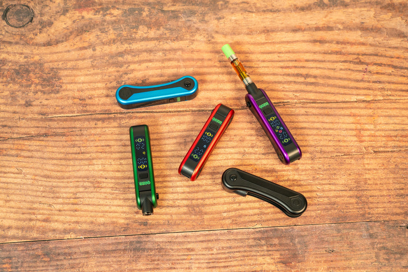 All 5 Hinge colors laying on a wood table. Some have the screen on and the purple's cart is open