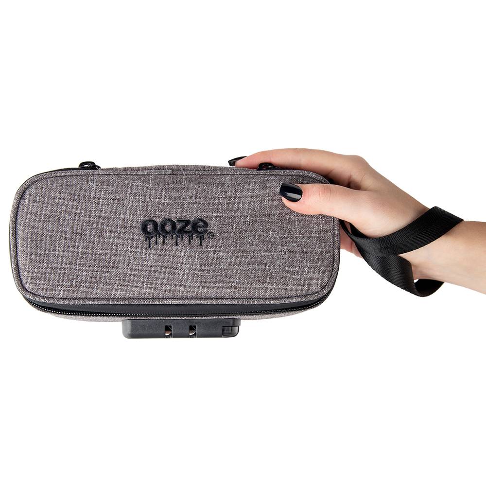A girl with black nails is holding a smoke gray Ooze smell proof travel kit while wearing the wrist strap