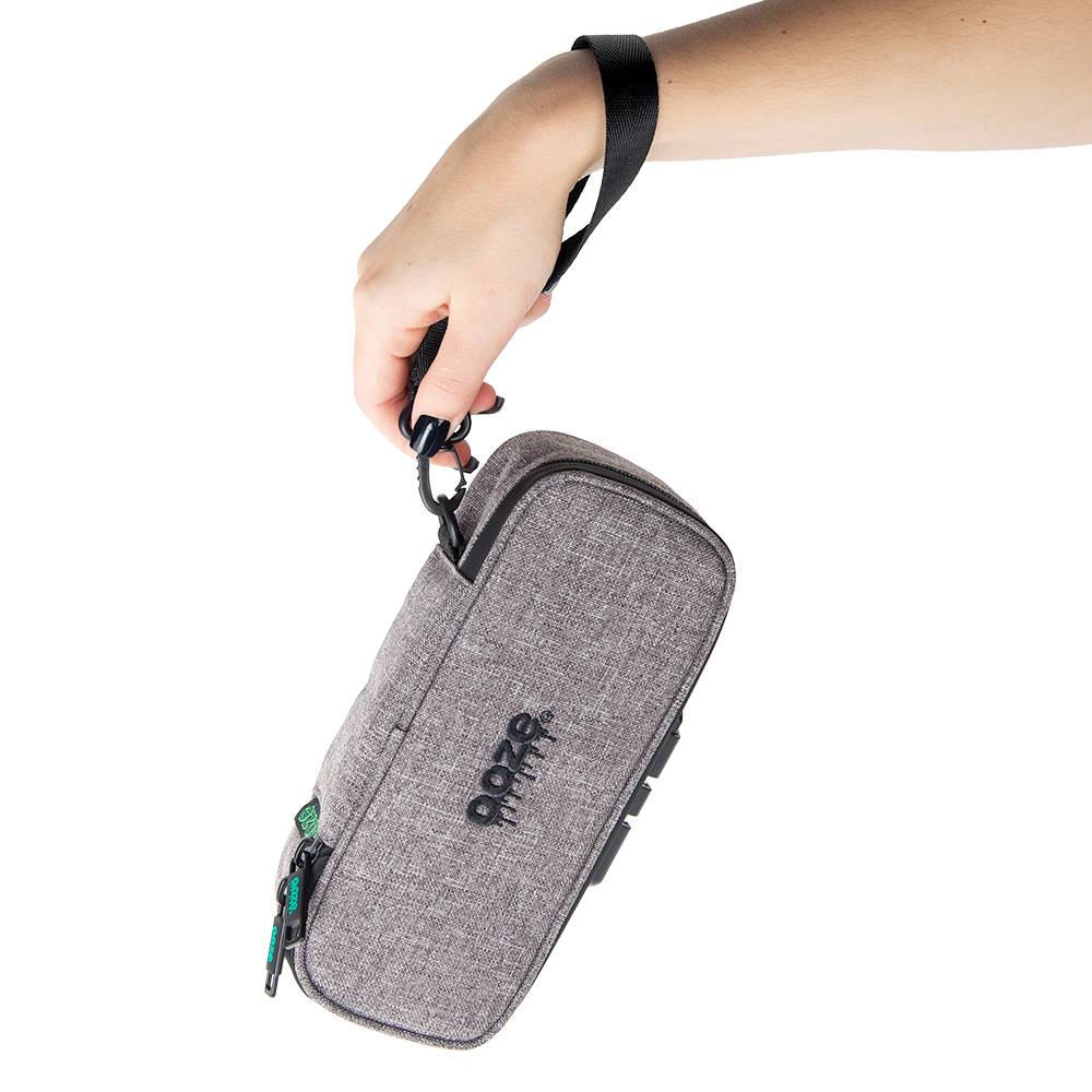 A girl with black and pink nails holds a closed smoke gray Ooze travel pouch by the wrist strap