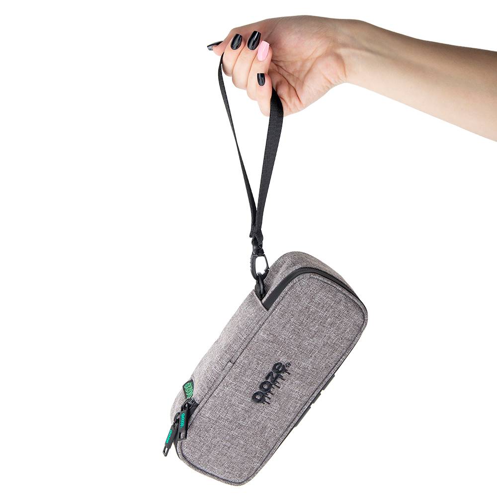 A girl with black and pink nails holds a closed smoke gray Ooze travel pouch by the wrist strap