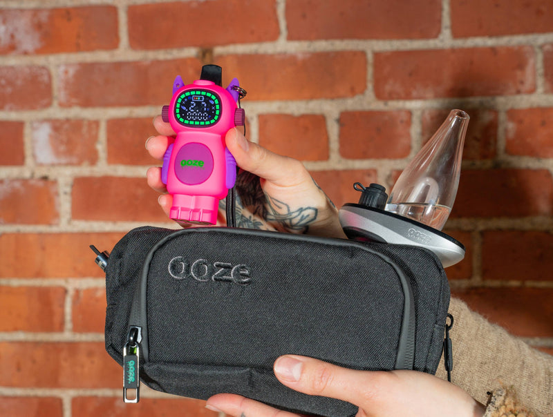 Holding an Atomic pink Ooze Bot character vape battery above a travel pouch