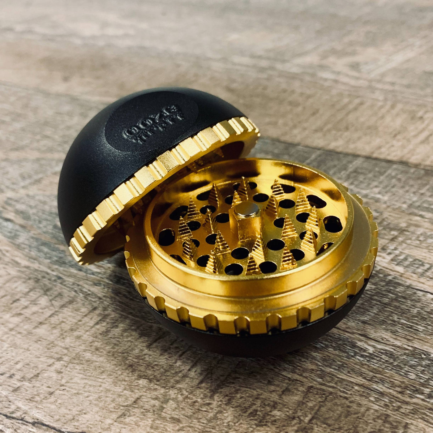A black saturn grinder sitting with the lid propped open to show the gold teeth