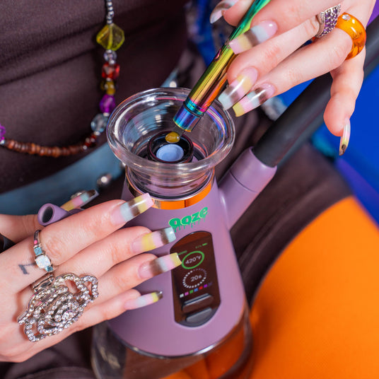 Person using a rainbow Hot Knife to load a dab into a purple Ripley dab hookah