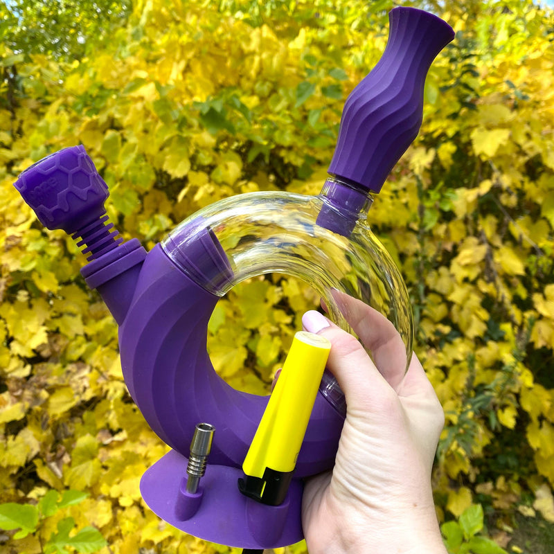Purple Ooze Ozone water pipe is held outside with the armor bowl inserted and a yellow lighter in a slot on the side