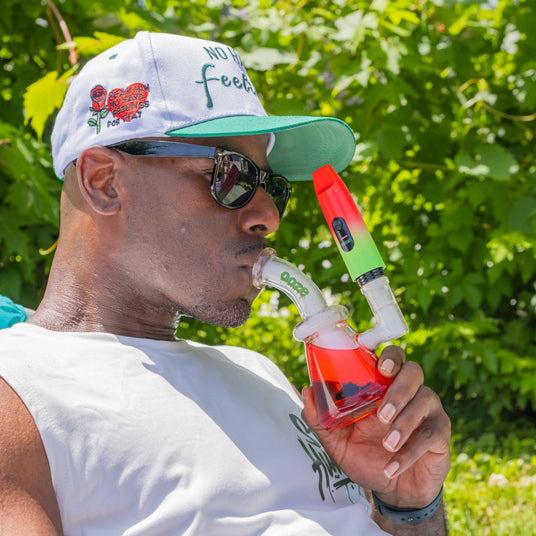 Man smoking from a colorful water pipe with greenery in the background