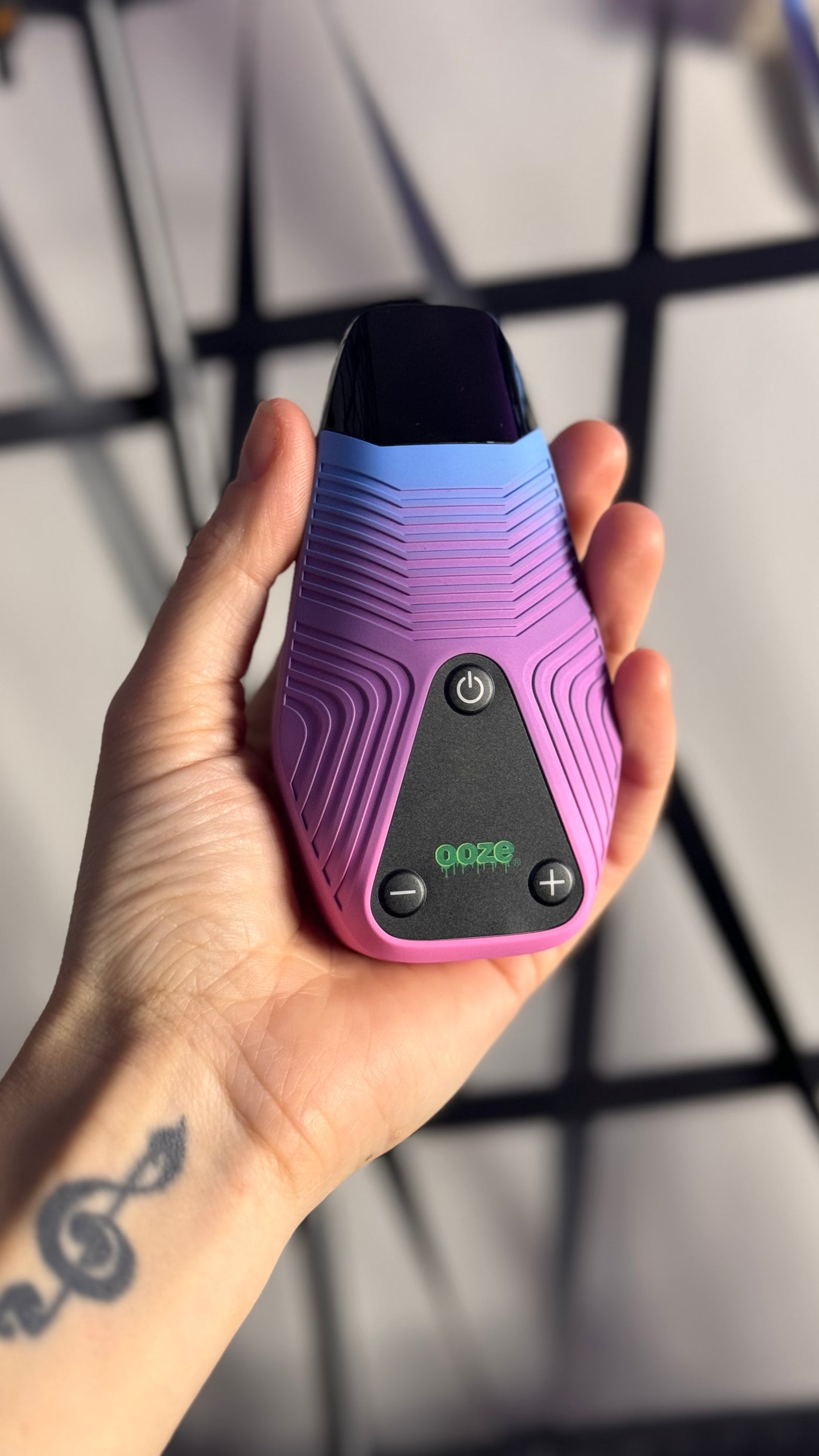 Person with tattoos holding Brink purple and blue vape with screen off