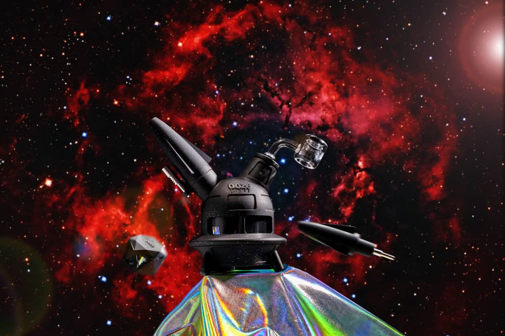 The shimmer black Ooze UFO is shown as a dab rig against a red black galaxy background with the dab straw and stash jar floating nearby