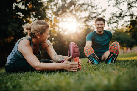 A fitness couple stretches outdoors in a park on the lawn. Young man and blonde woman in workout clothes getting ready to exercise