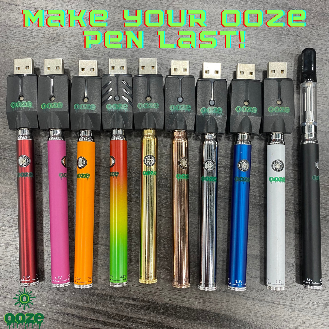A group of Ooze Slim Twist Batteries in all different colors are laying flat on a gray wood table. All the batteries have the smart usb charger attached except for the black battery that has an empty cartridge on the very right.