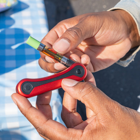 Close-up of hands holding a red Hinge battery with a green-tipped cartridge.