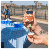 Person holding a Hoot owl vape device with a checkered pattern outdoors, near a table with blue cups.