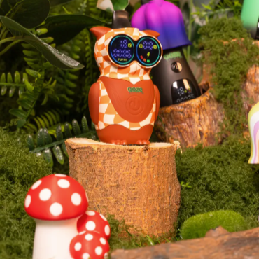 Owl device with digital display on a log surrounded by plants and mushrooms