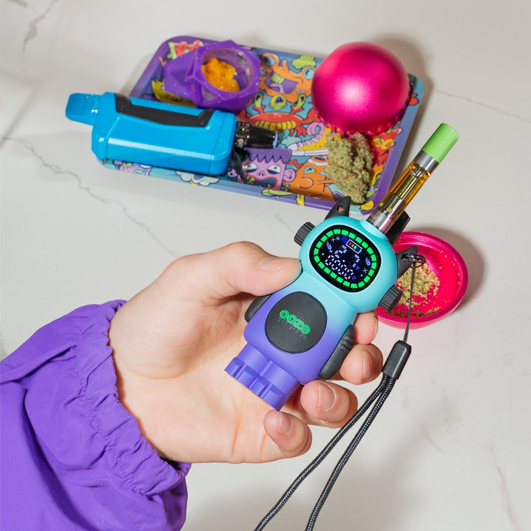 Hand holding a moonrise Bot device with a background of various items on a white surface