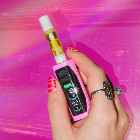 Close up of a hand with pink nails holding  pink Ooze Runt mini battery against a pink background