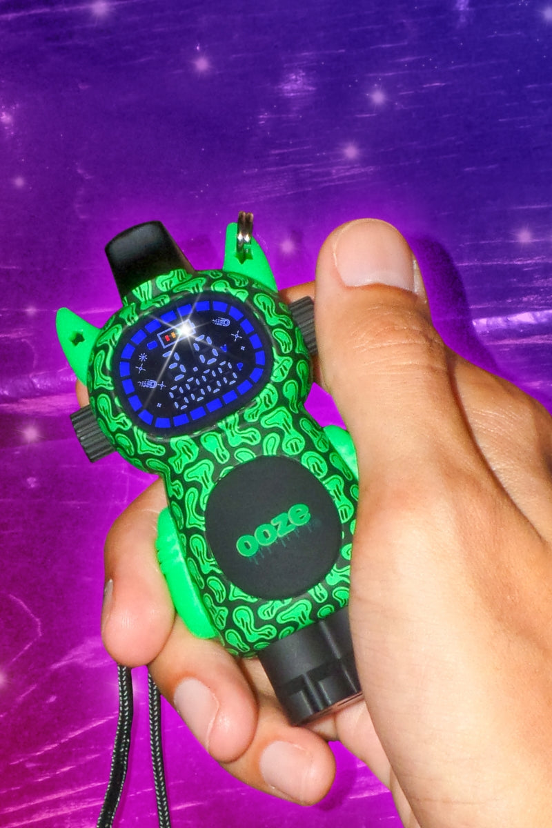 Close up of a hand holding the melty design Ooze Bot character vape against a sparkly purple background