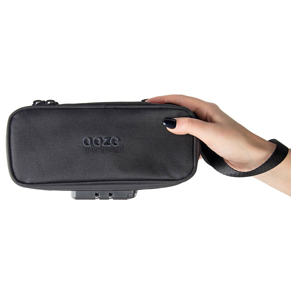 A girl with black nails is holding a closed black Ooze travel kit while wearing the wrist strap