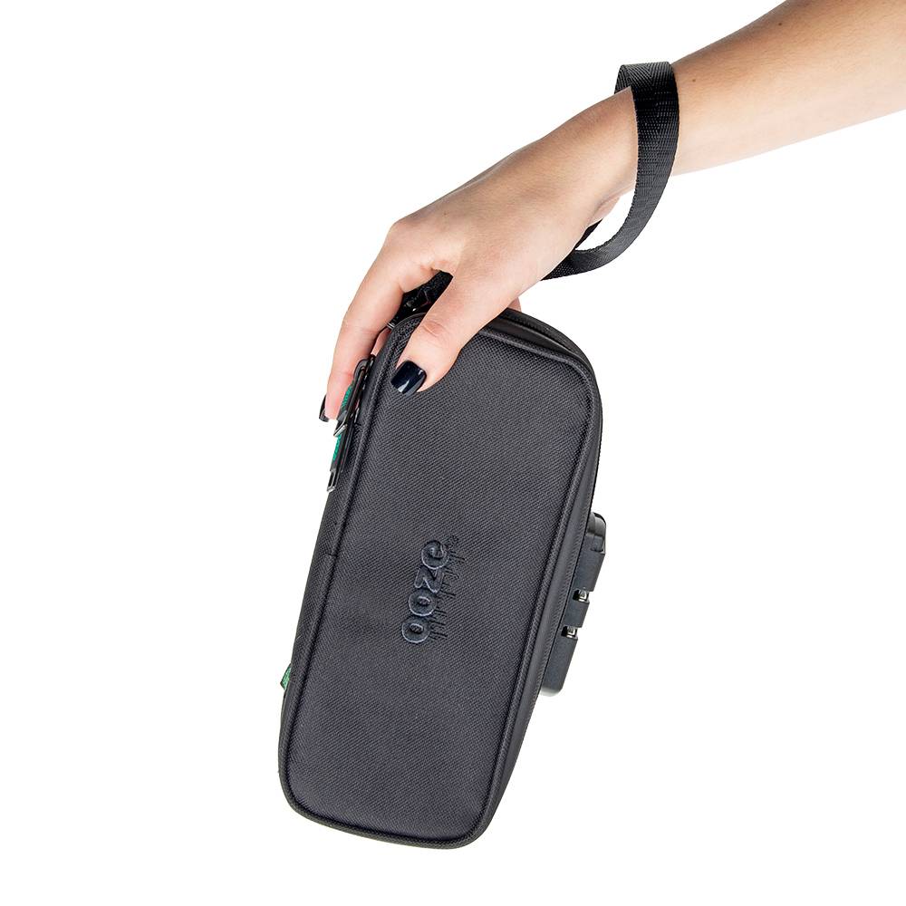 A girl with black nails is holding the black Ooze travel kit at a downward angle while wearing the wrist strap