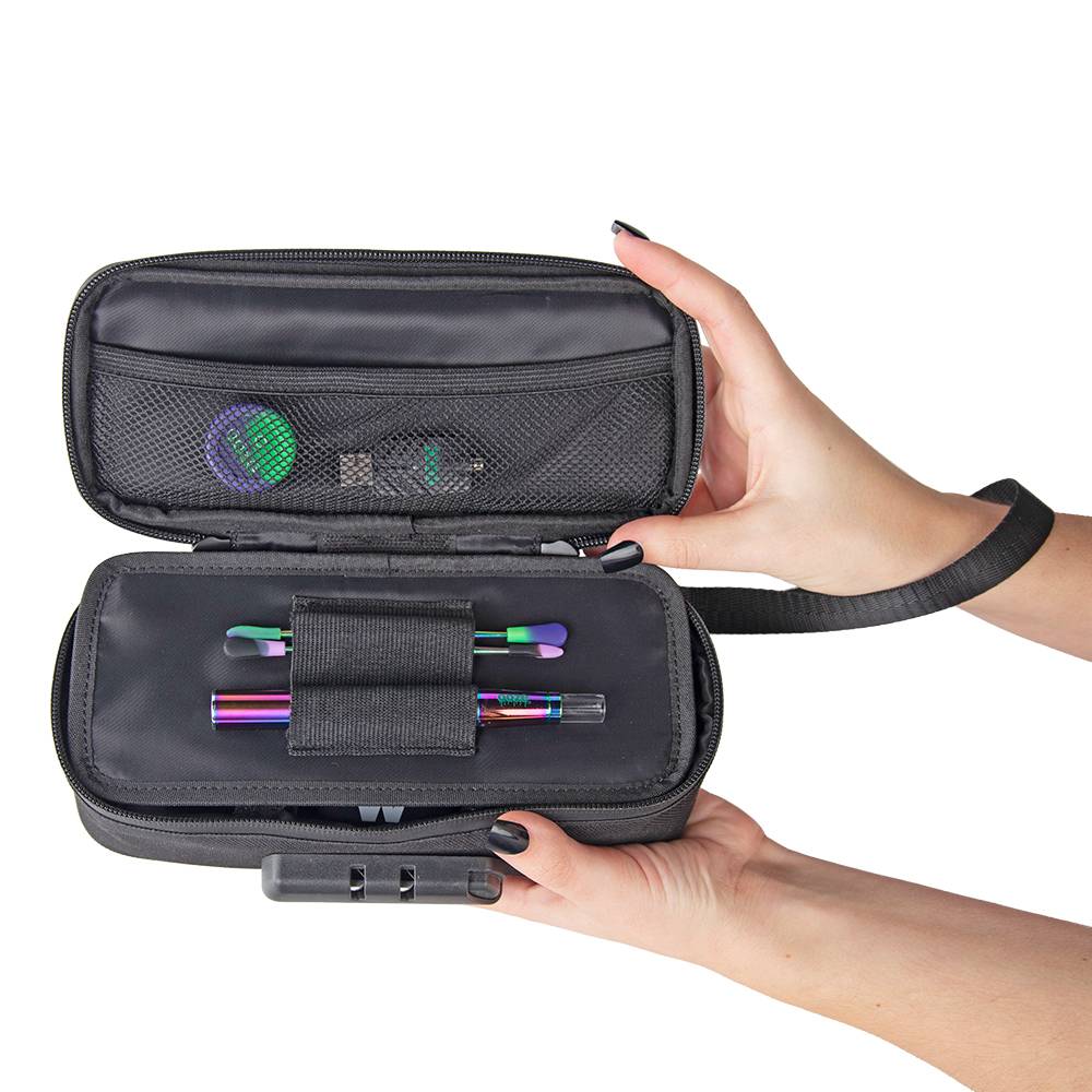A girl with black nails is holding the black Ooze travel pouch open to show an Ooze pen and two dab tools, a silicone stash jar and a charger all stored inside