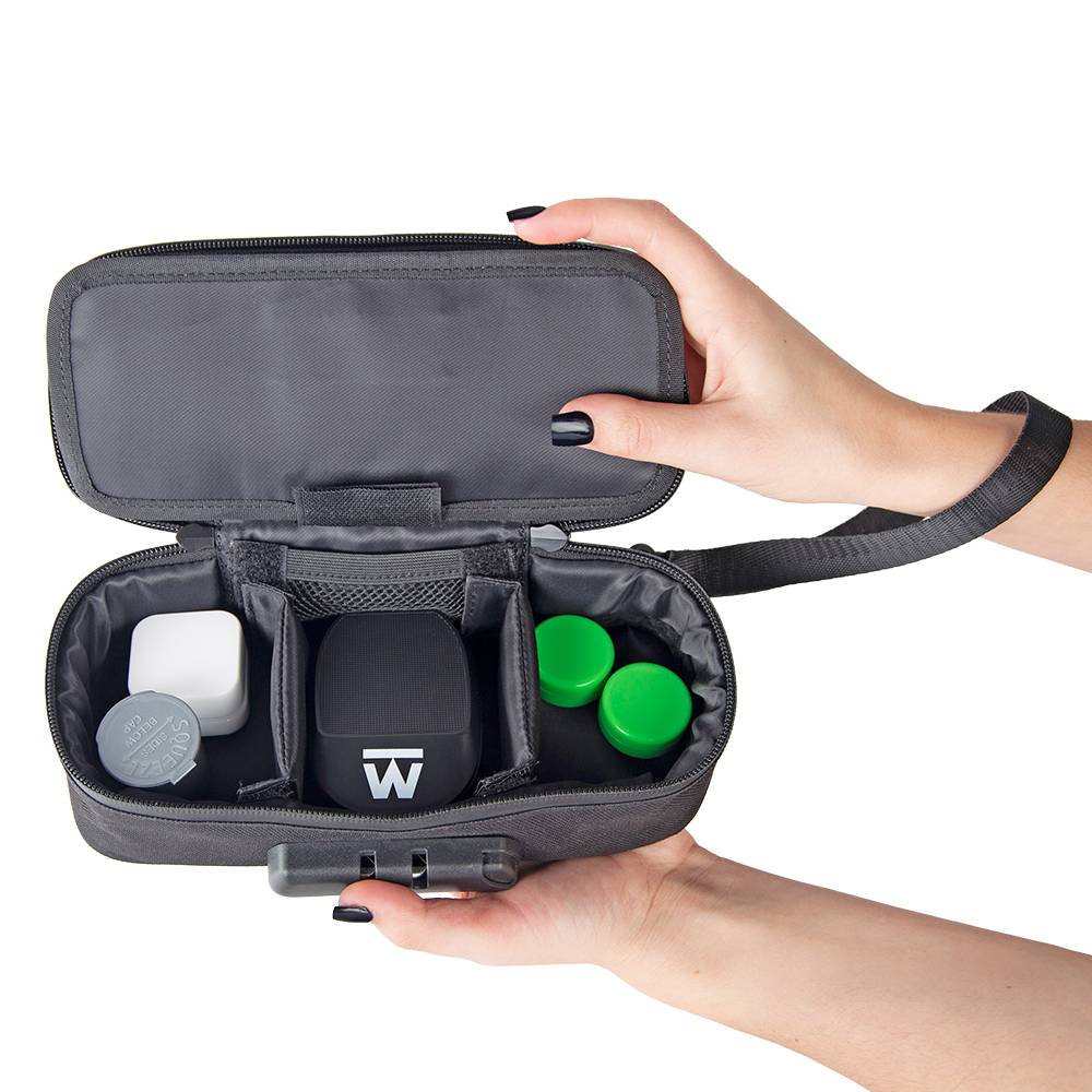 A girl with black nails is holding a black Ooze travel kit open to show a variety of storage containers and a small Truweigh scale.