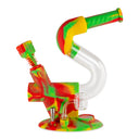 A colorful Ooze Swerve silicone water pipe designed in a 'Z' shape with red, yellow, and green segments, featuring a glass dab rig attachment and a dab straw, on a matching rasta-colored base.