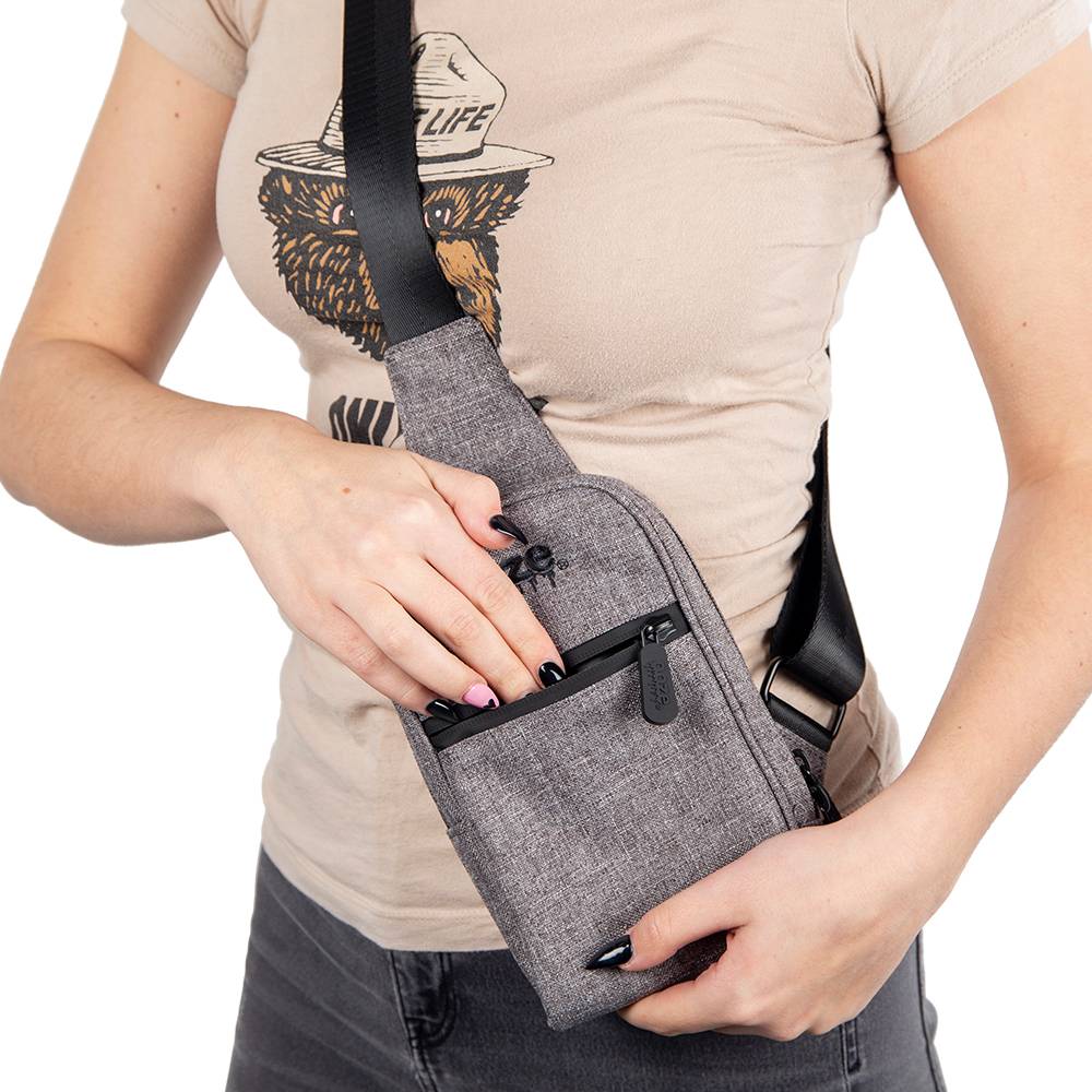 A girl wearing the grey Ooze crossbody bag has her hand sticking into the front pocket