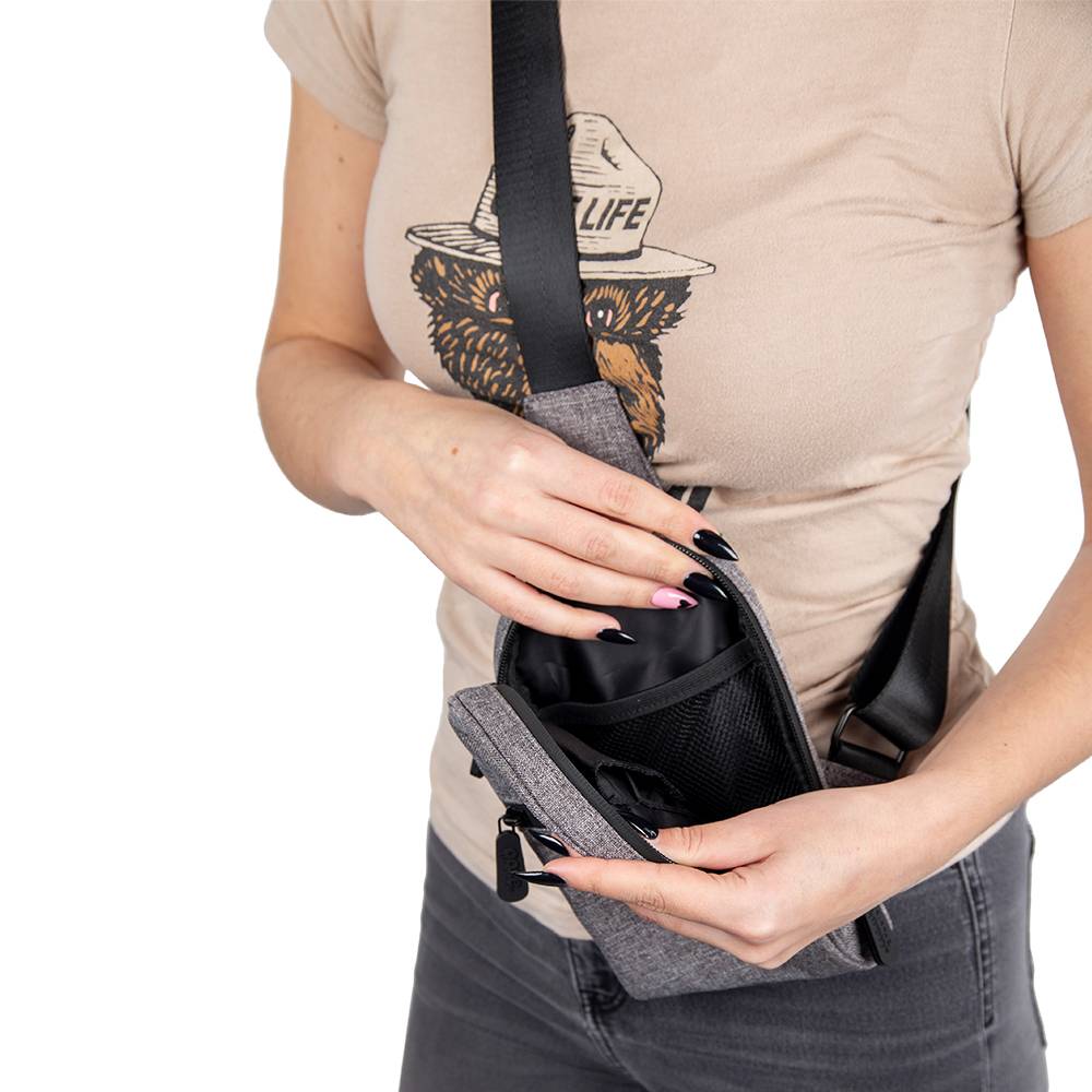 A girl is wearing the smoke grey Ooze crossbody bag. It's unzipped and she's holding it open to show the black lining