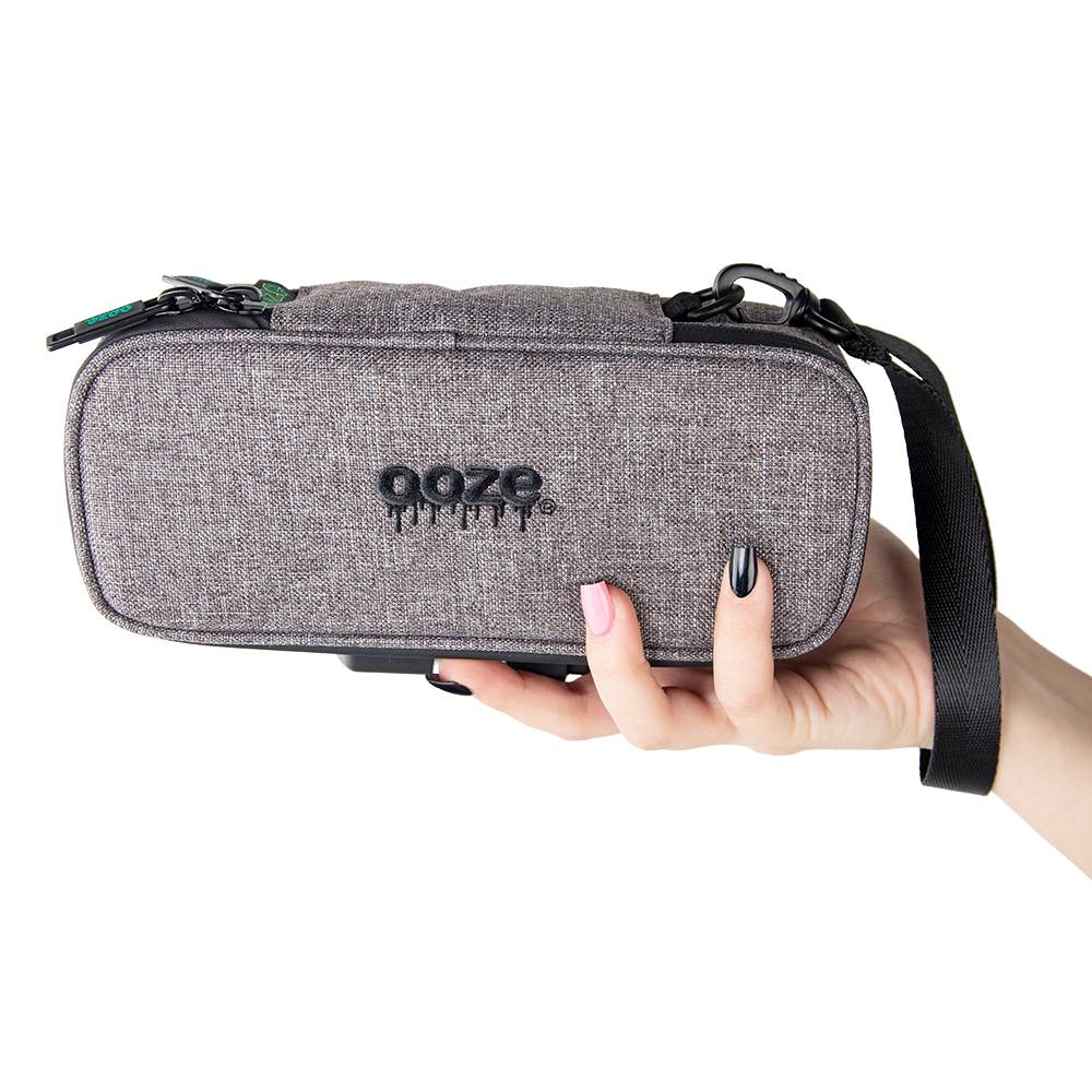 A girl with black and pink nails is holding up a smoke grey Ooze travel kit