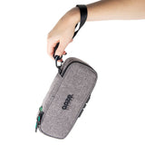 A girl with black and pink nails holds a closed smoke gray Ooze travel pouch by the wrist strap