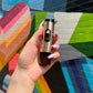A girl's hand with long lilac acrylic nails is holding the Black Rose Ooze Booster in front of a colorful wall mural.