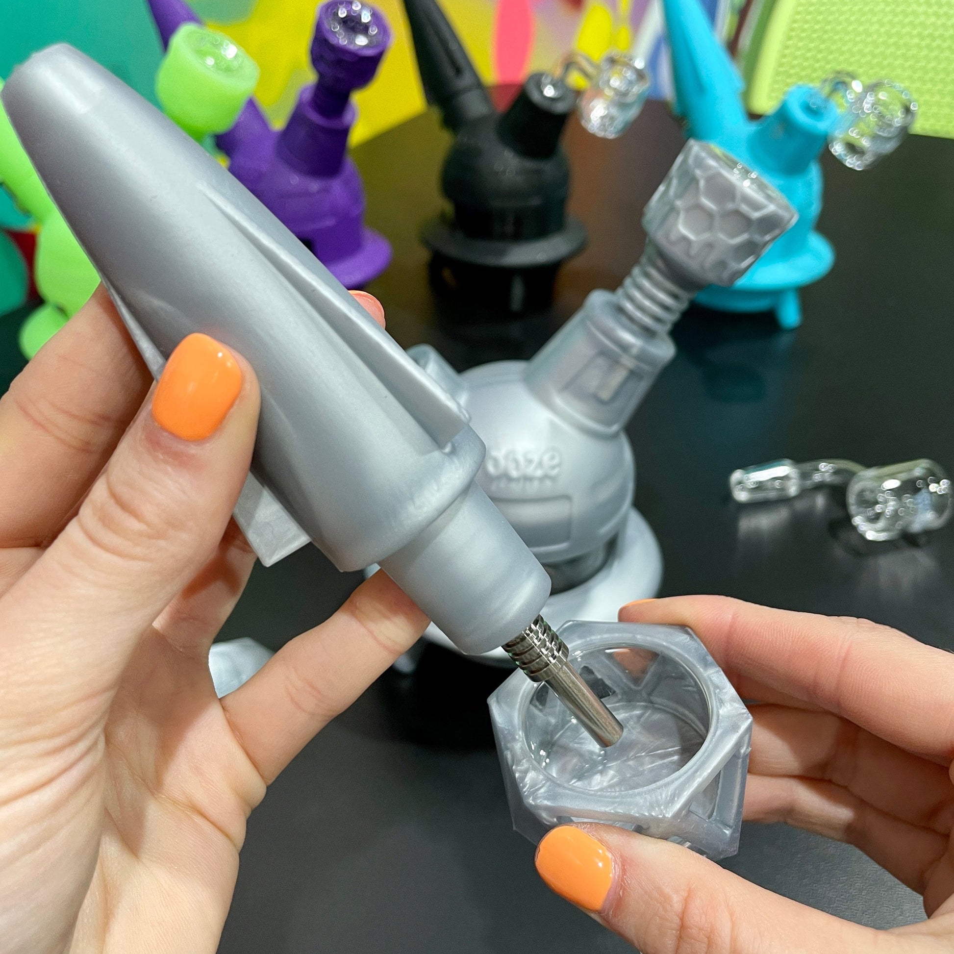 A girl is using the silver Ooze UFO as a dab straw with the titanium nail inserted into the matching Geode stash jar