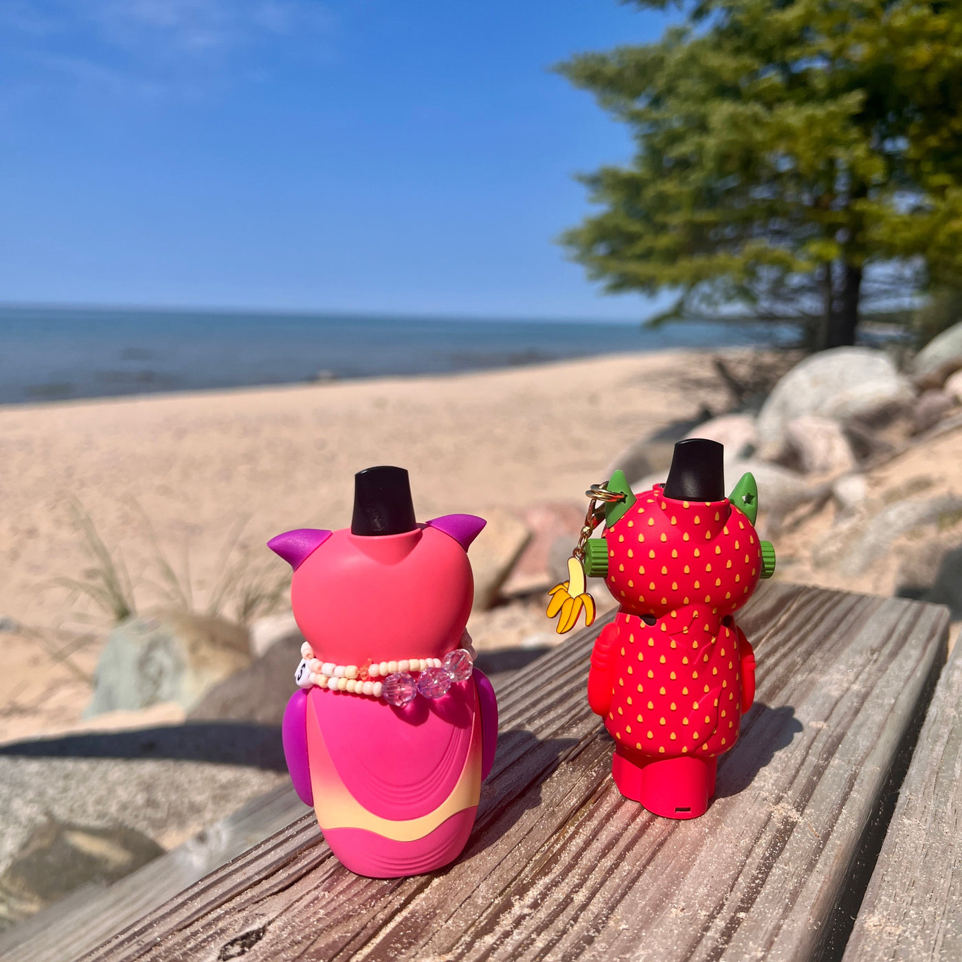 Two colorful figurines on a wooden surface with a beach and tree in the background