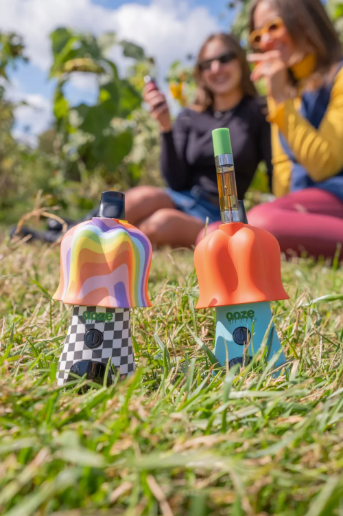 Trip mode and electric cherry Shroom vape batteries in the grass, one has a cart connected to the top