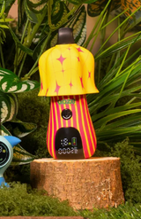 Mushroom shaped device with start and stripe circus pattern, placed on a wooden stump with green foliage in the background.