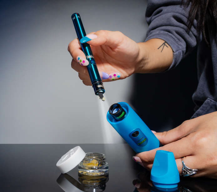 Using a hot knife to load a dab into a blue Booster wax vape.