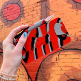 Hand holding a red, gray and black Ooze Slugger silicone dab dugout with the straw on top against a mural wall background