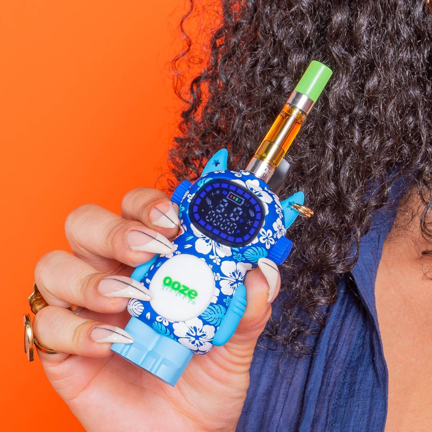 Person holding a blue Ooze Bot vape device against an orange background