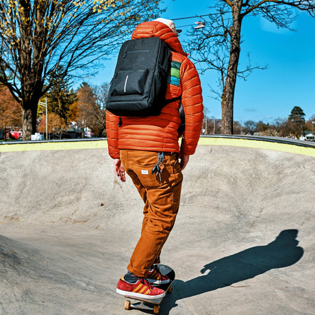 Guy in an orange jacket and pants with a black Ooze backpack skateboarding in a bowl