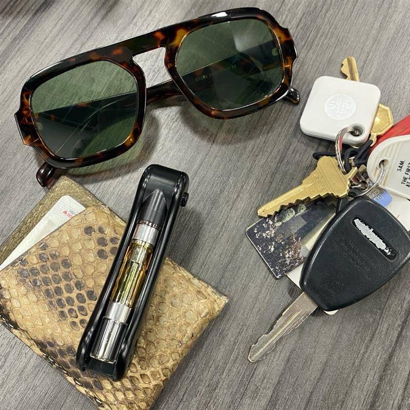 Sunglasses, black Hinge vape pen, wallet, keys on a wooden surface