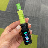 Close up of a person holding the black Ooze Runt Mini Battery with the screen turned on and a cartridge with a green tip and foam cover attached