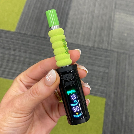 Close up of a person holding the black Ooze Runt Mini Battery with the screen turned on and a cartridge with a green tip and foam cover attached