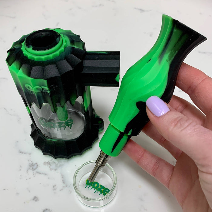 The mouthpiece of the black and green Ooze Clobb silicone bong is pulled out with the titanium nail connected, aimed to take a dab out of a glass dish