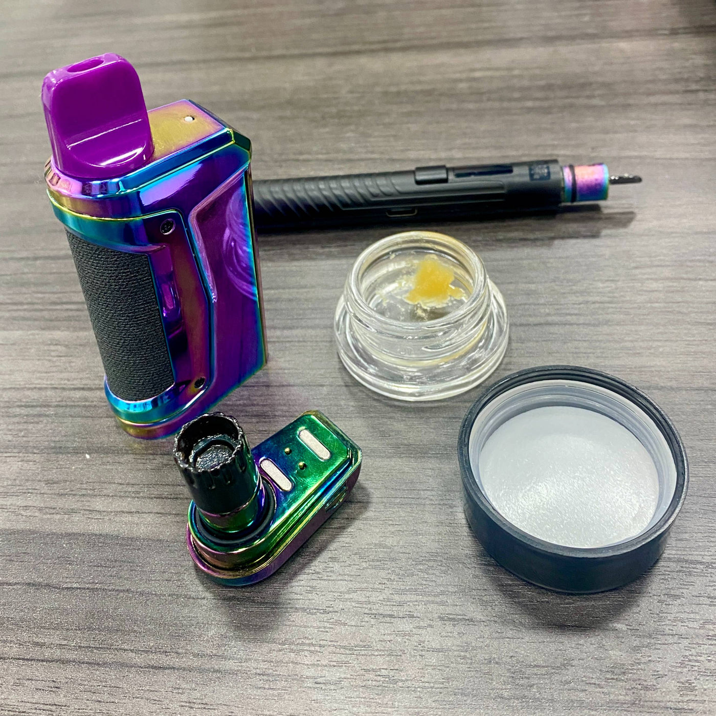 A rainbow Duplex 2 has the base pulled out with a dab in the Onyx Atomizer. An open jar of wax and black hot knife are next to the device.