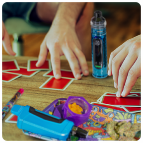 Friends at game night playing a card game with an Ooze Titan Extract Vaporizer and other Ooze products on the table.