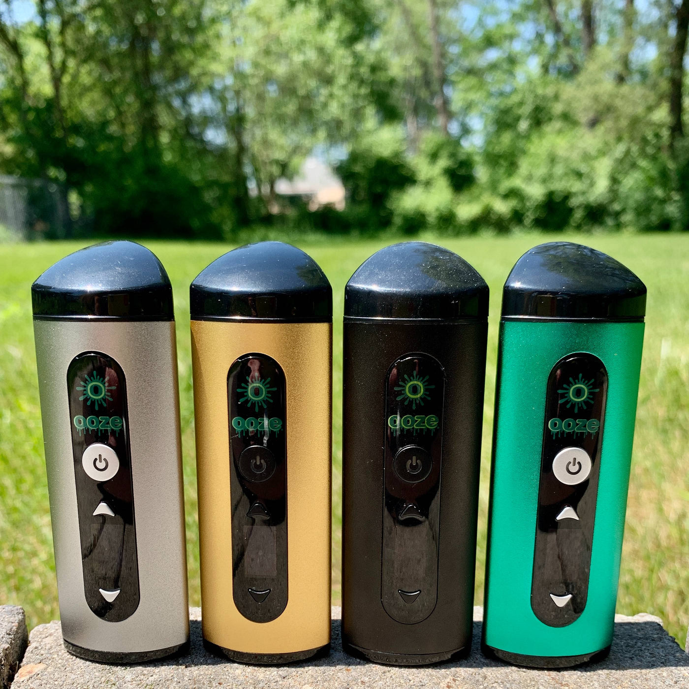Silver, gold, black, and green Ooze Drought dry herb vapes are lined up outside