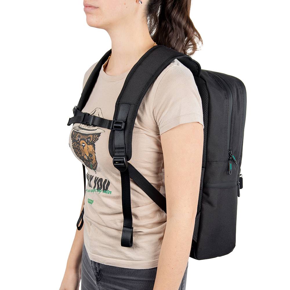 A girl is wearing a tan Ooze shirt and the black Ooze backpack with the straps buckled across her chest