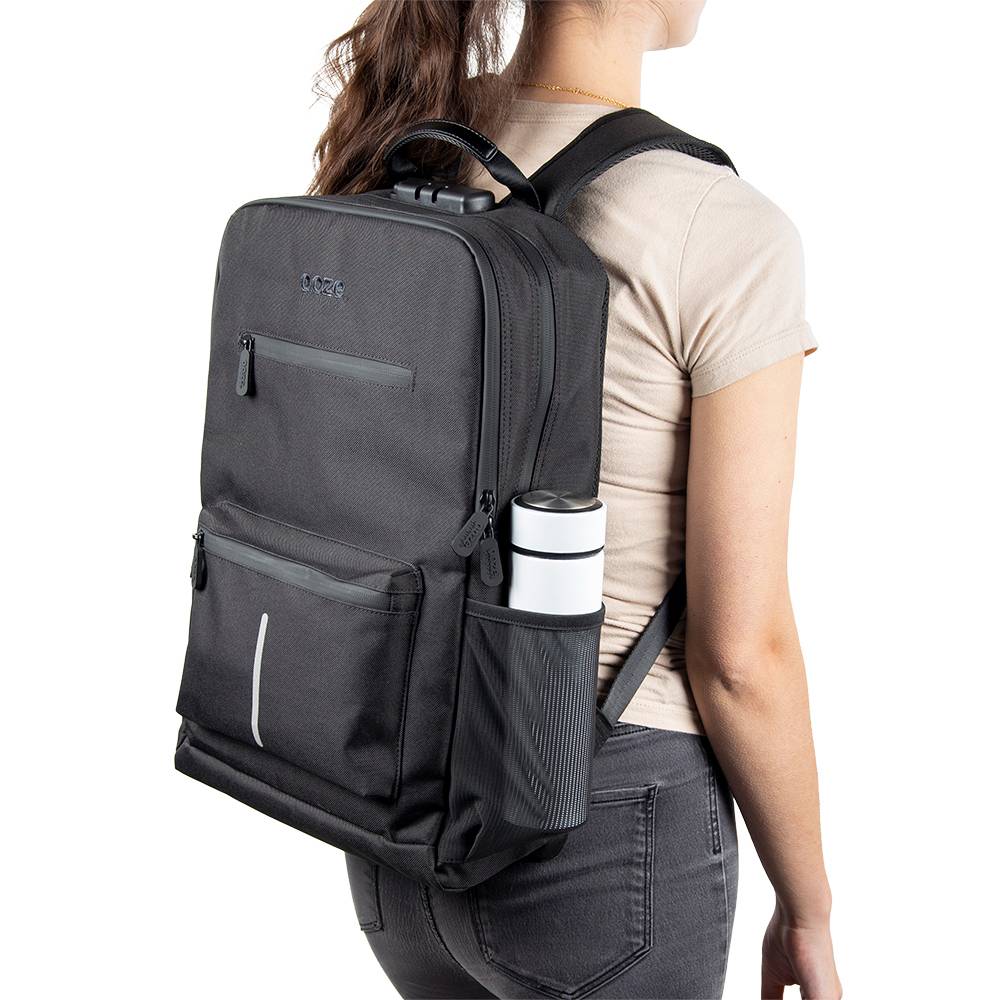 A girl is wearing the black Ooze backpack with a white water bottle in the side pocket