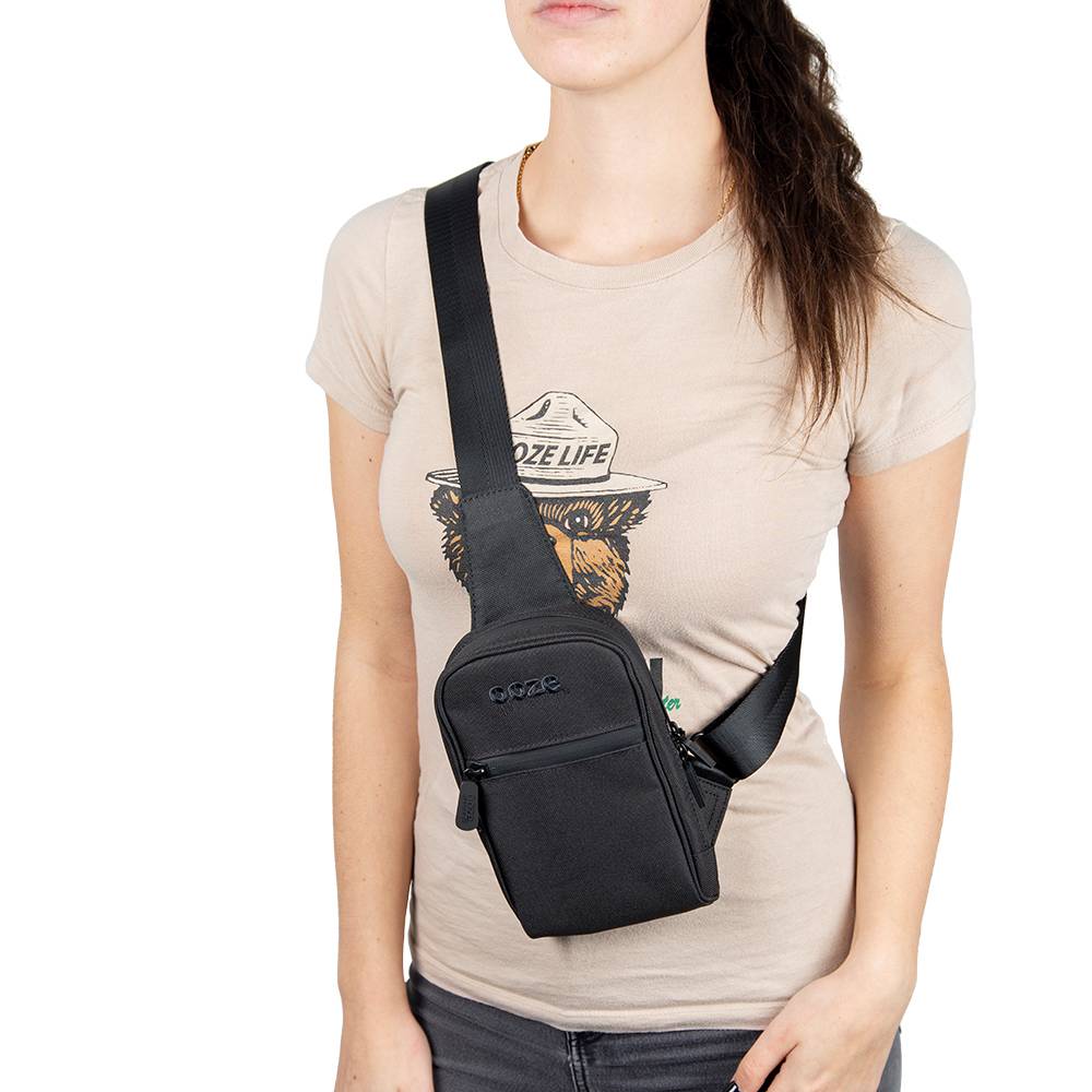 A brunette is wearing a tan shirt and the black Ooze crossbody bag across her chest