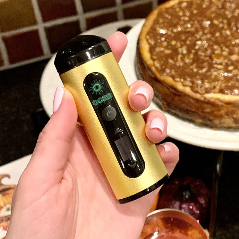 Person holding a gold Drought dry herb vape with a pie in the background
