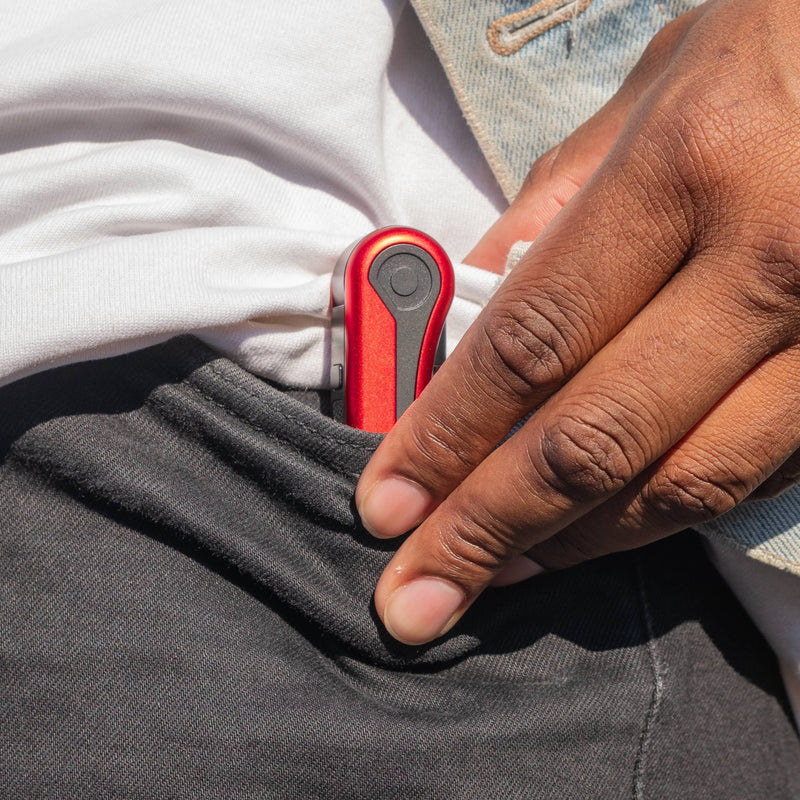 Hand pulling a red Hinge battery out of a black denim pants pocket